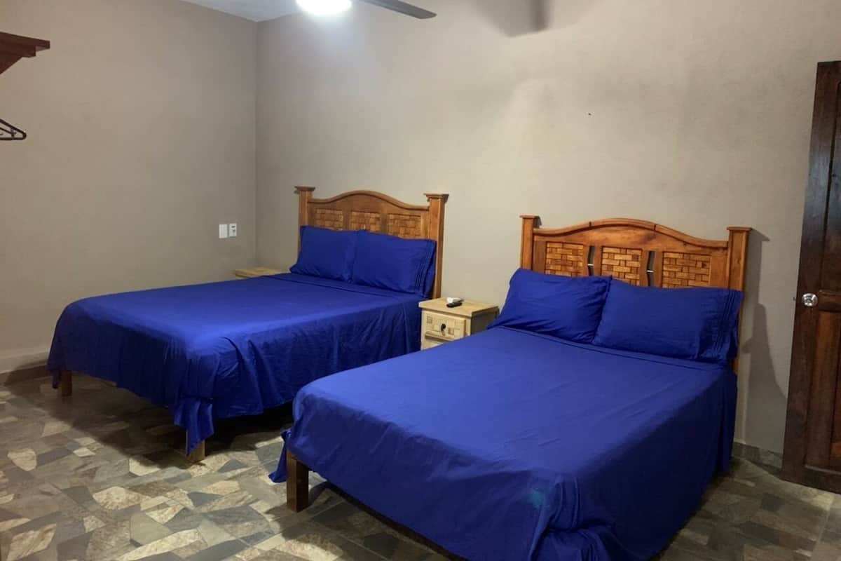 A room with two wooden beds with headboards, a small wooden nightstand, and a ceiling fan.