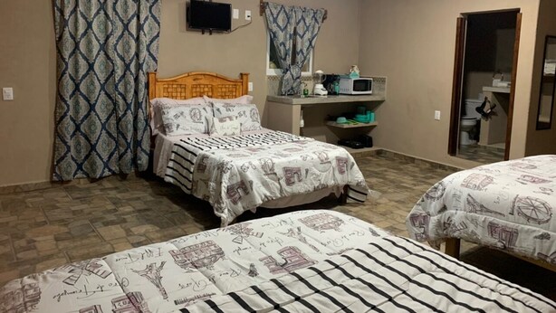 A bedroom with two beds, a ceiling fan, an air conditioner, and a small kitchenette area. - Bungalows Victoria (La Manzanilla)