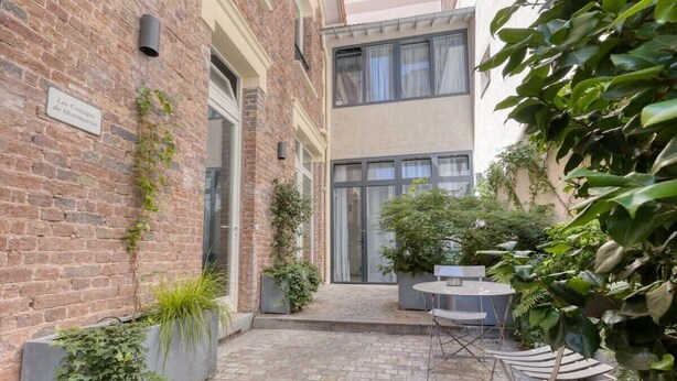 A courtyard with a brick wall, potted plants, and outdoor seating. - Cute & Bright Studio in a Courtyard-Montmartre(5) (Paris)