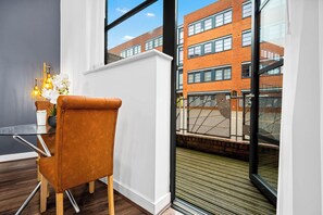 A modern room with a glass table, a brown leather chair, and a view of a brick building through a large window. - Luxury Studio -  Balcony -  City Centre -  JQ (Birmingham)