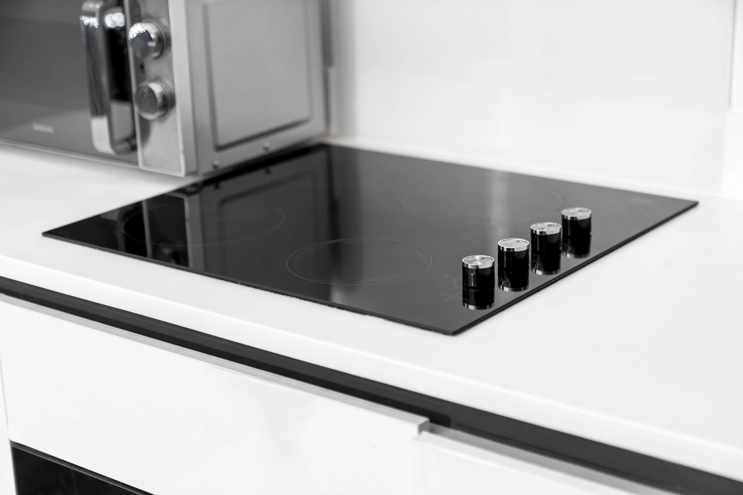 A kitchen with a black induction cooktop and four black knobs.