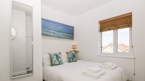 Ein Schlafzimmer mit einem Bett, Kissen, einem Gemälde, einem Fenster und einer Lampe.