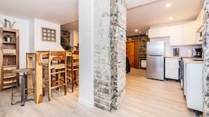 A modern kitchen with white cabinets, a built-in refrigerator, and a stone accent wall. - Modern Meets Rustic - 2 Bdrm Old Quebec (Québec City)