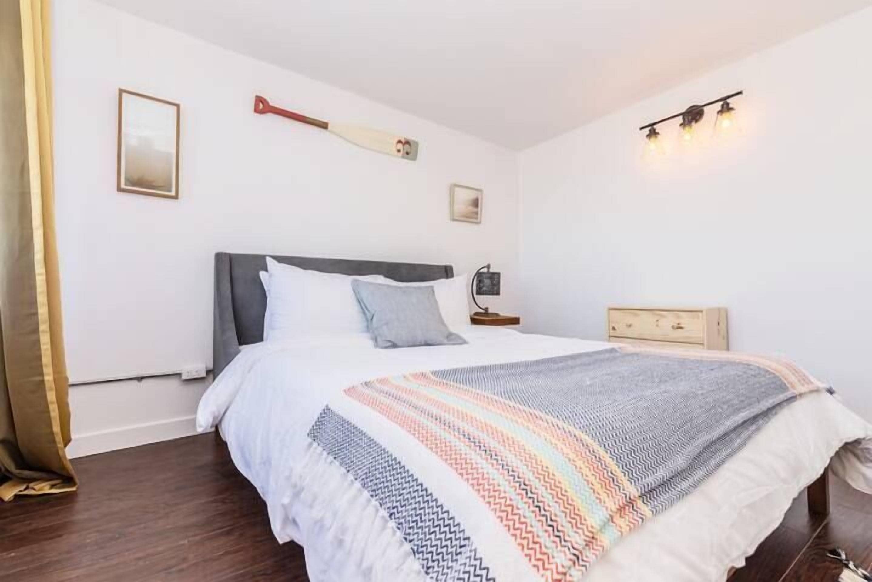 Un dormitorio ordenado con cama, mesitas de noche y una lámpara fijada a la pared.
