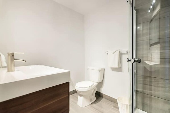 A modern bathroom with a white sink, toilet, and shower area. - Modern Meets Rustic - 2 Bdrm Old Quebec (Québec City)