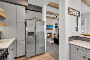 A modern kitchen with a stainless steel refrigerator, white cabinetry, and a 'let's eat' sign on the wall.