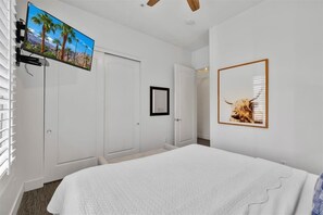 A bedroom with a bed, a mounted TV, a framed picture of a cow, and white walls. - The Luxe Loft A | 1BR Legacy Villa (La Quinta)