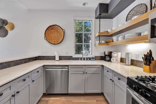 A modern kitchen with grey cabinets, a dishwasher, a stove, and a window providing natural light.