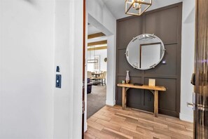 A modern interior with a wooden floor, a round mirror on a dark wall, and a small wooden table with a vase. - The Luxe Loft A | 1BR Legacy Villa (La Quinta)