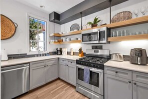Een moderne keuken met grijze kastjes, een roestvrijstalen fornuis, een magnetron en houten planken.