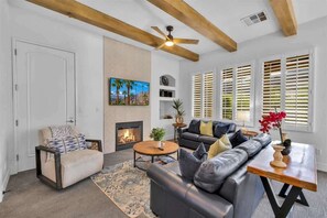 A living room with a fireplace, a sofa, a coffee table, and a ceiling fan. - The Luxe Loft A | 1BR Legacy Villa (La Quinta)