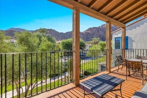 A balcony with a view of mountains, a patio with a table and chairs, and a building with blue shutters.