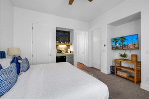 Ein Schlafzimmer mit einem großen Bett, einem Fernseher und einer Küchenzeile im Hintergrund.