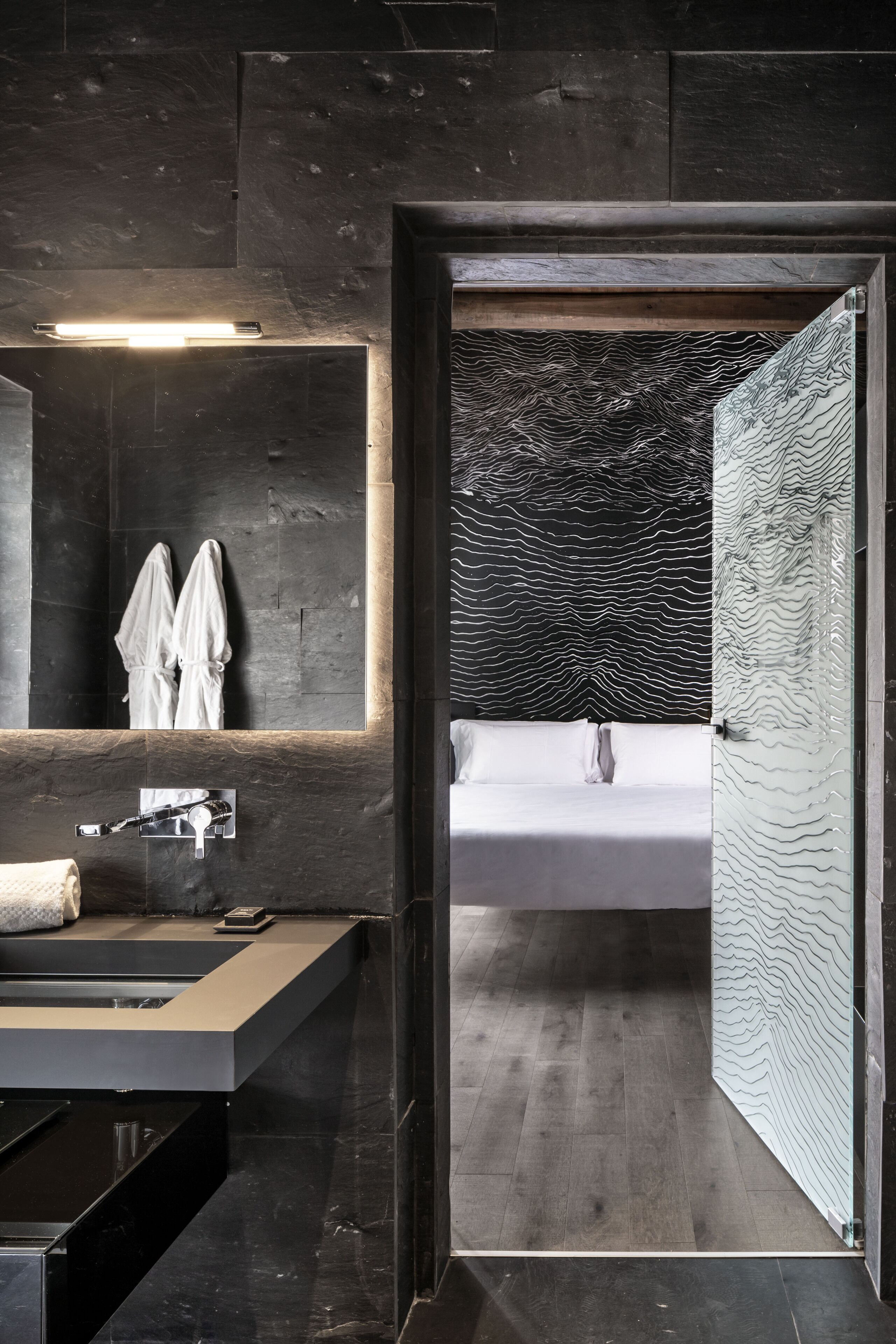 Un bagno moderno con pavimento in legno scuro, uno specchio grande, un lavandino e una vasca da bagno bianca.