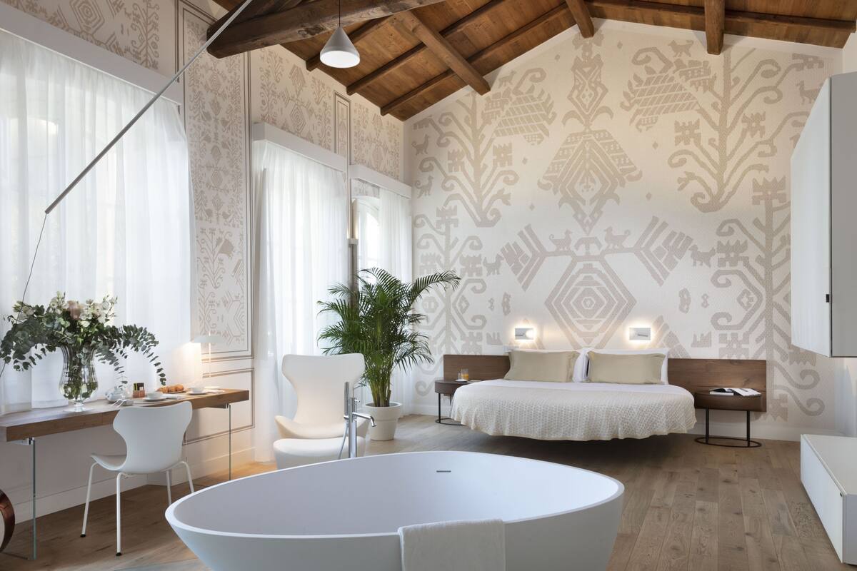 Ein modernes Schlafzimmer mit einem großen Bett, einem Schreibtisch mit Stuhl, einer Zimmerpflanze und einer Badewanne.