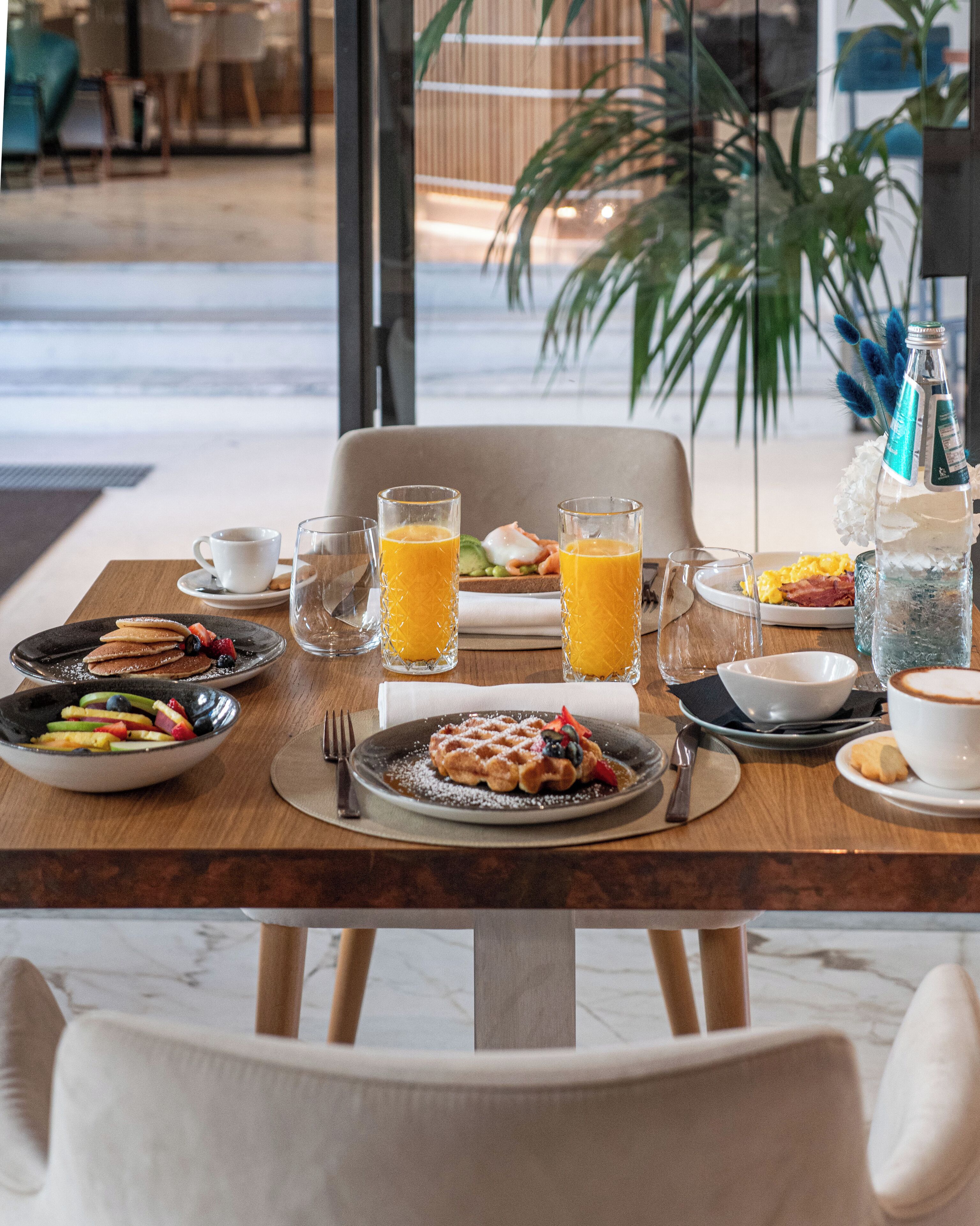 Una mesa de desayuno con platos de comida, vasos de jugo de naranja y una botella de agua.