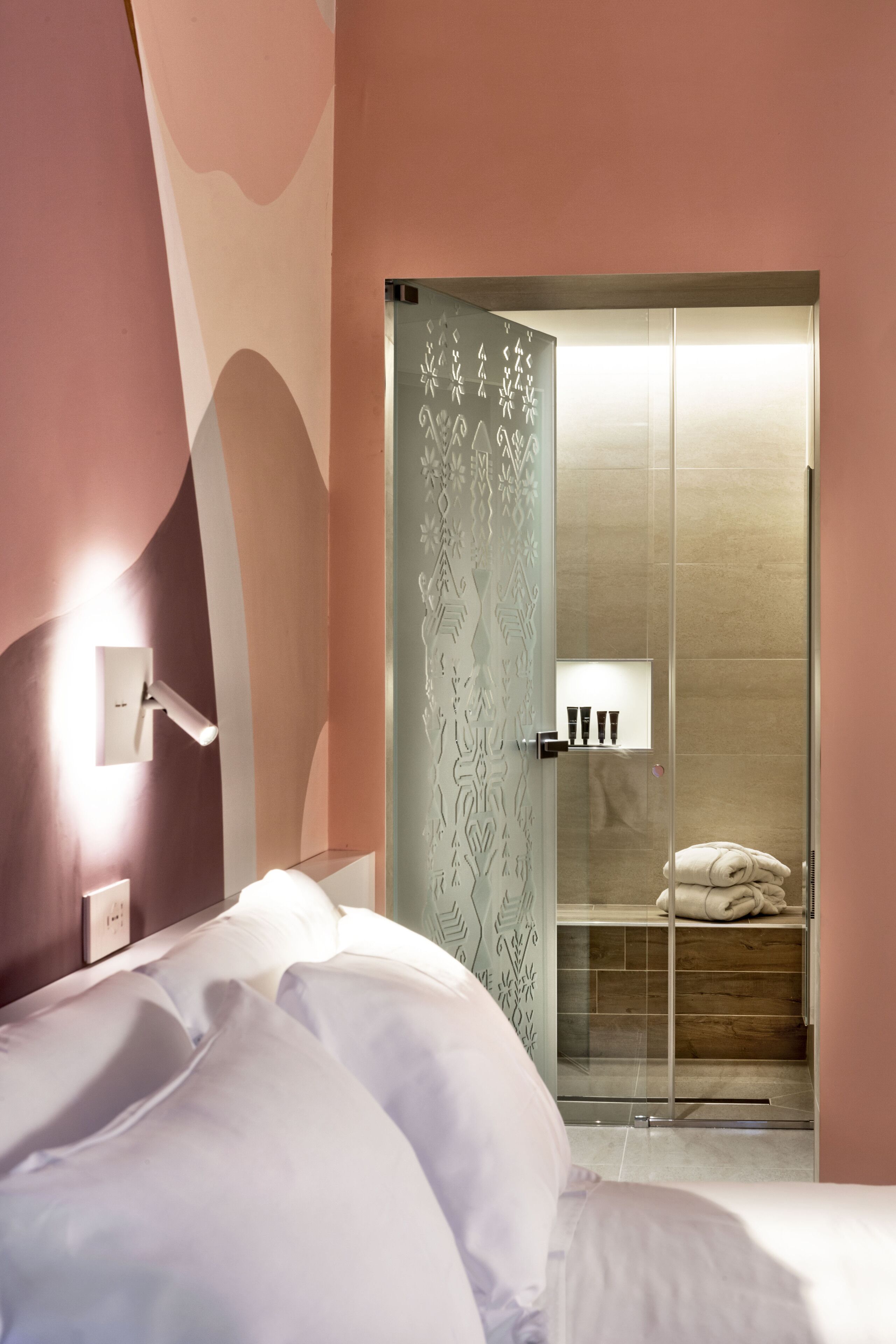 A modern bedroom with a bed, bedside table, and a glass-enclosed shower area.