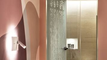 A modern bedroom with a bed, bedside table, and a glass-enclosed shower area.