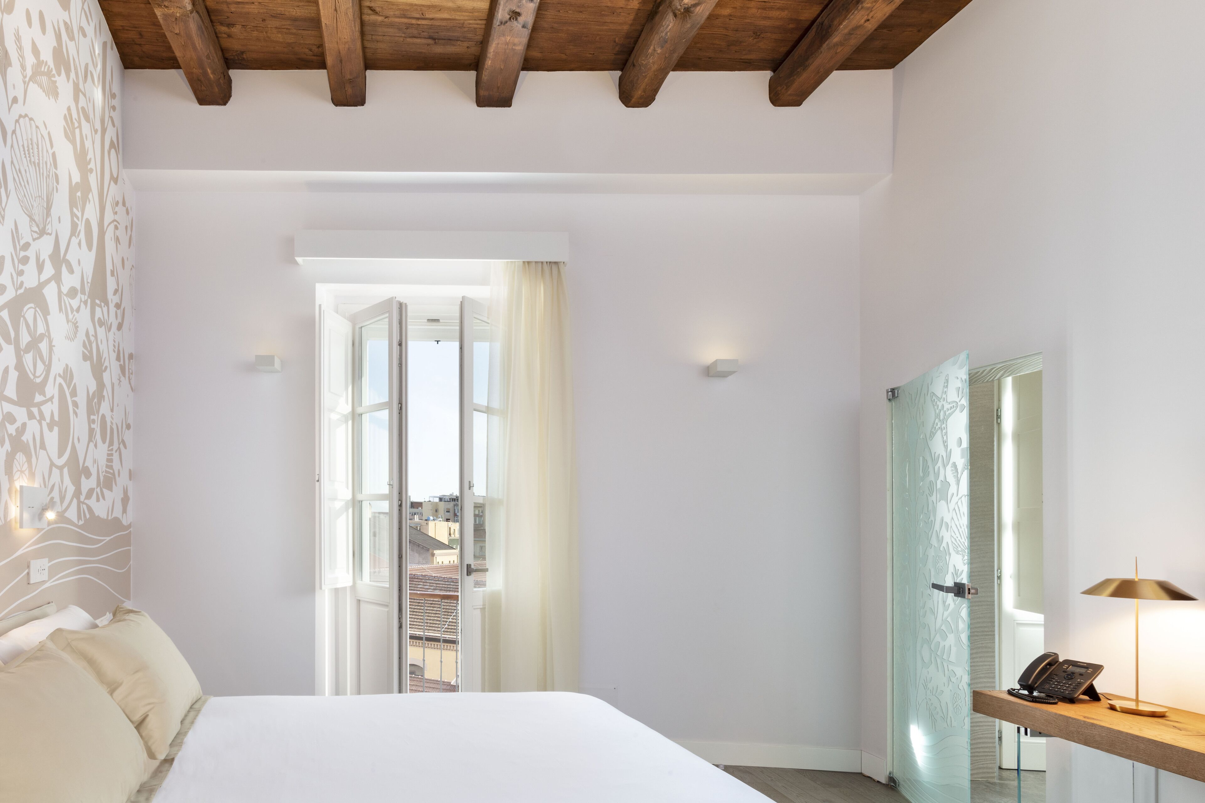 Ein Schlafzimmer mit einem Bett, einem Schreibtisch mit Lampe, einem Telefon und einer Tür, die auf einen Balkon führt.
