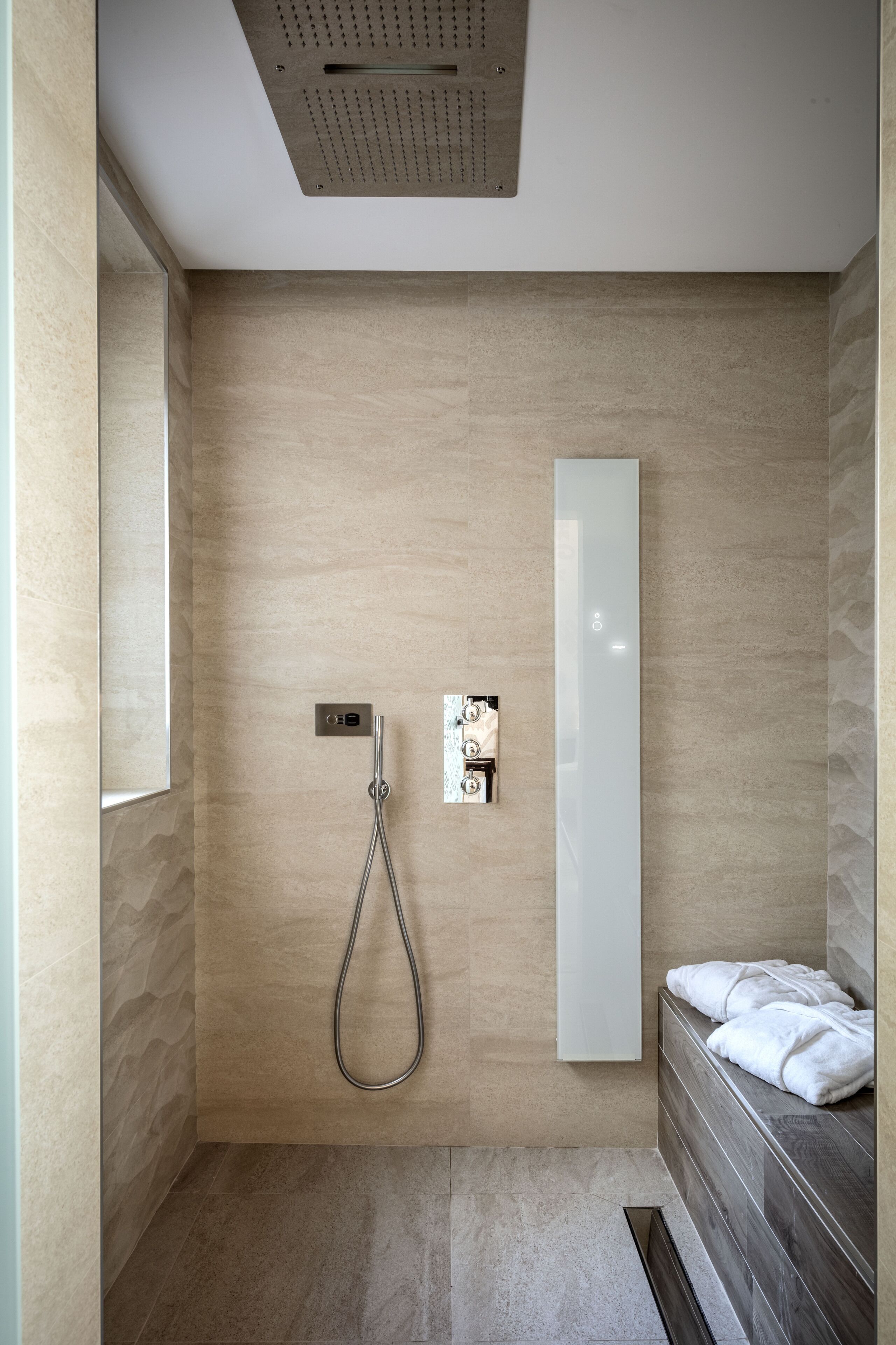 Ein modernes Badezimmer mit Dusche, einem großen Spiegel und einer integrierten Sitzbank.