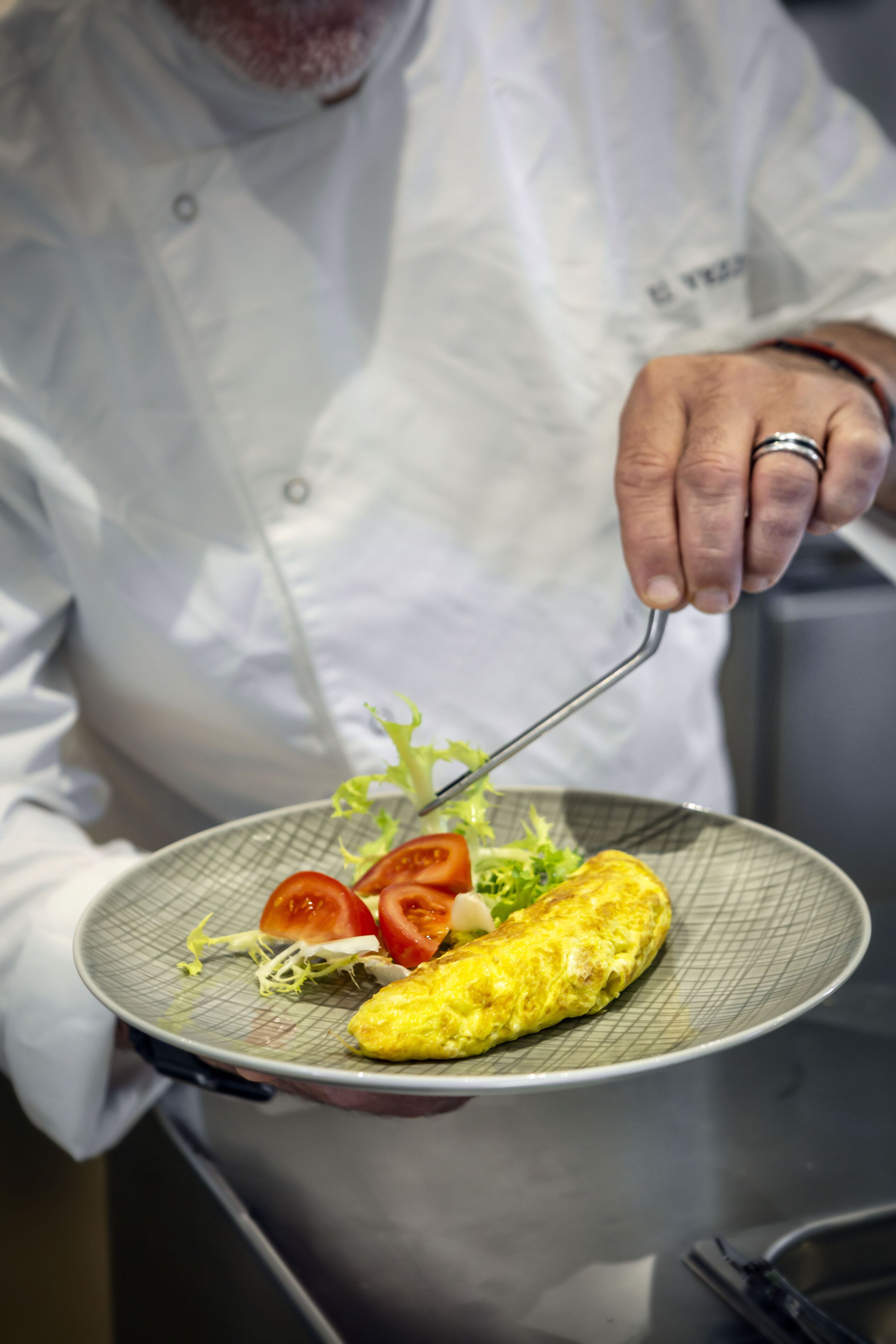 Un chef tenant une assiette avec une omelette et des légumes.