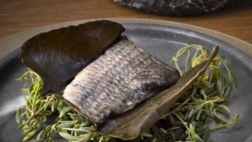 A stone plate with a fish, herbs, and a dark bowl with a sauce garnish.
