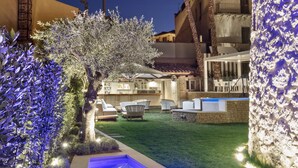 A nighttime view of a hotel courtyard with a swimming pool, palm trees, and a stone wall. - Casa Clàt – Boutique Hotel (Cagliari)