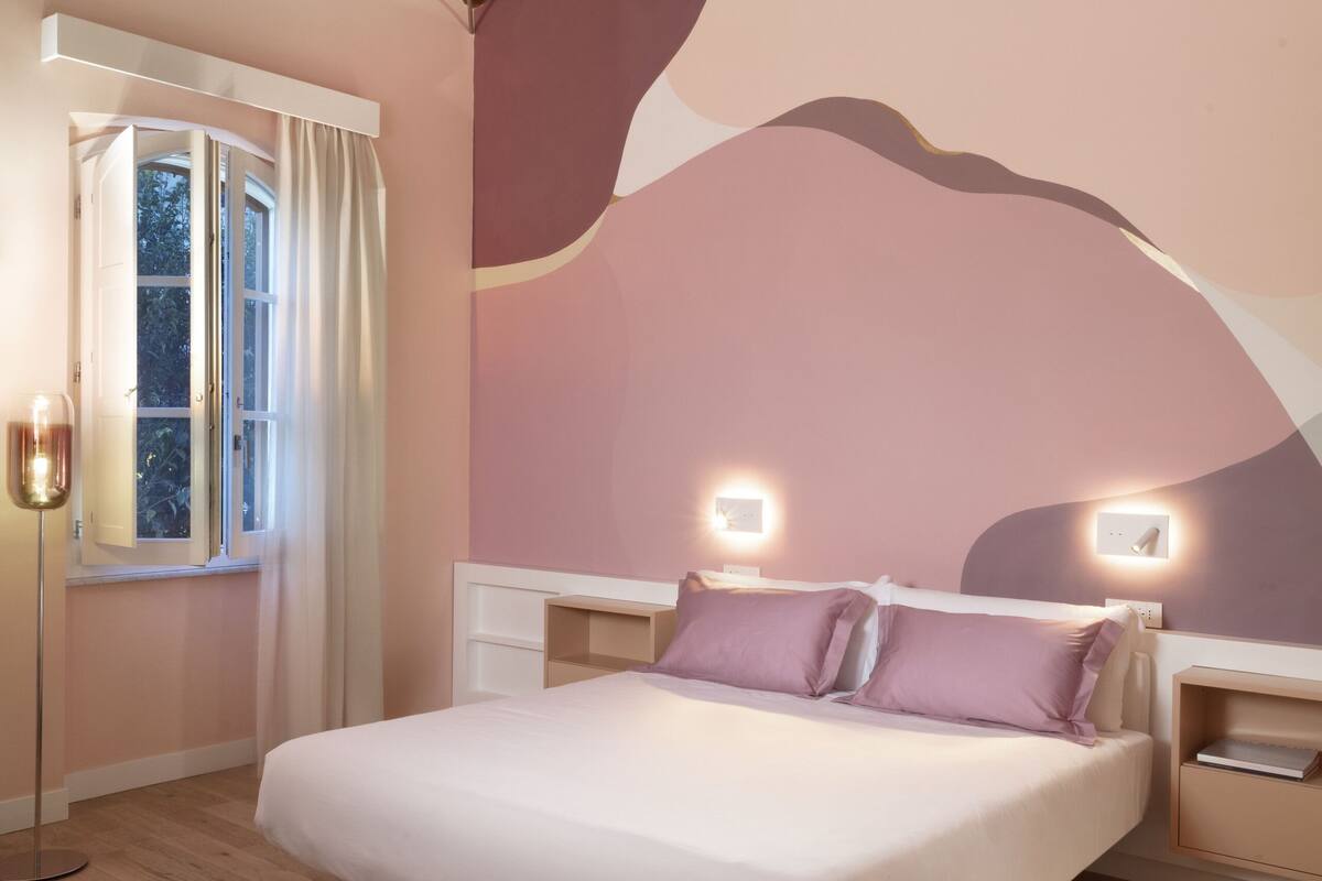Ein Schlafzimmer mit Holzboden, einem großen Bett, Nachttischlampen und einem Fenster mit Vorhängen.