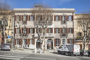 Un edificio de varios pisos con estilo arquitectónico clásico, que presenta una entrada central con dosel y un área de estacionamiento al frente.