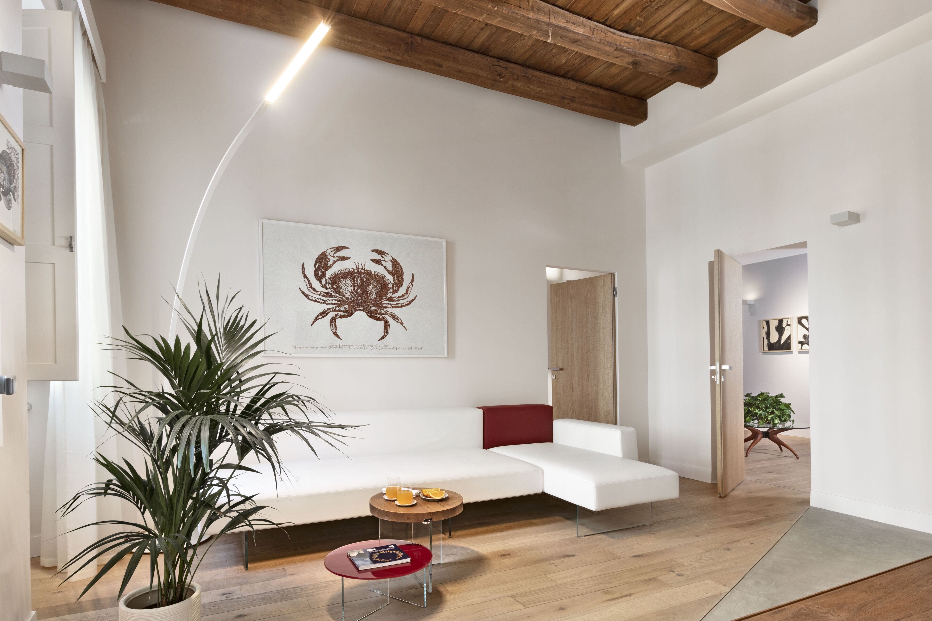Een moderne woonkamer met een witte bank, een grote potplant, een klein rond tafeltje met een rode dienblad en een kunstwerk in een lijst aan de muur.