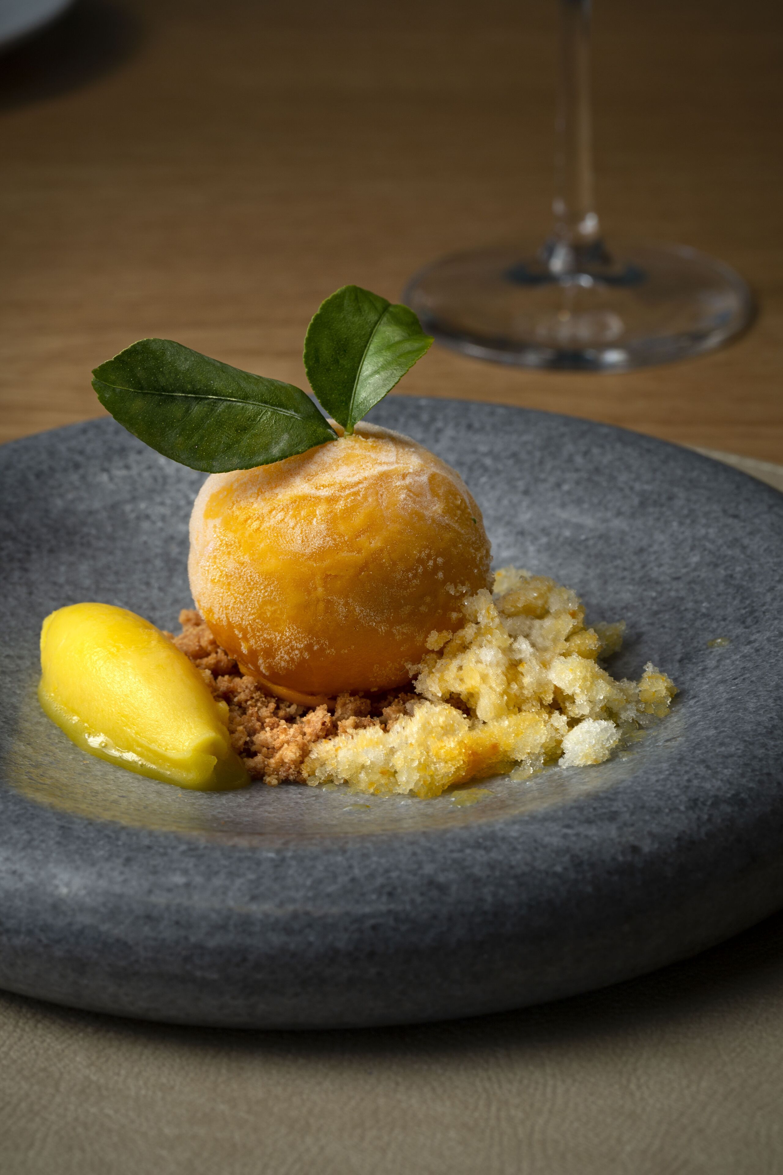 Un postre sobre un plato gris, con una copa de vino al fondo.