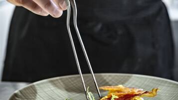 Una persona sosteniendo unas pinzas sobre un plato con huevos revueltos, tocino y una ensalada.