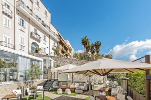 Una terraza en la azotea con mobiliario exterior, un muro de piedra y vistas a un edificio con balcones.