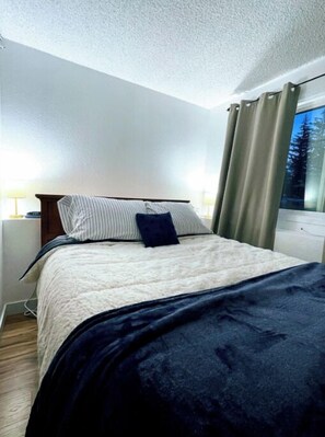 Enjoy a restful stay in this serene hotel room with a comfortable bed and a view of the surrounding trees.