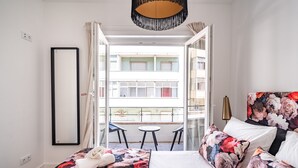 A hotel room with a bed, a small table, and a balcony with a view of the building. - Keluak Apartment, Wifi, Balcony !new! (Lisboa)