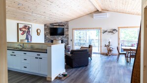 A spacious living area with a kitchen, dining area, and a stone fireplace. - Woodhaven Country Lodge (Oak Bay)