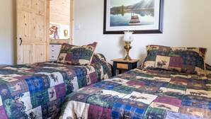 A bedroom with two beds, a wooden door, a framed picture on the wall, and a bedside table with a lamp. - Woodhaven Country Lodge (Oak Bay)