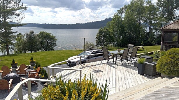 A wooden deck with outdoor seating, overlooking a lake and forested hills. - Woodhaven Country Lodge (Oak Bay)