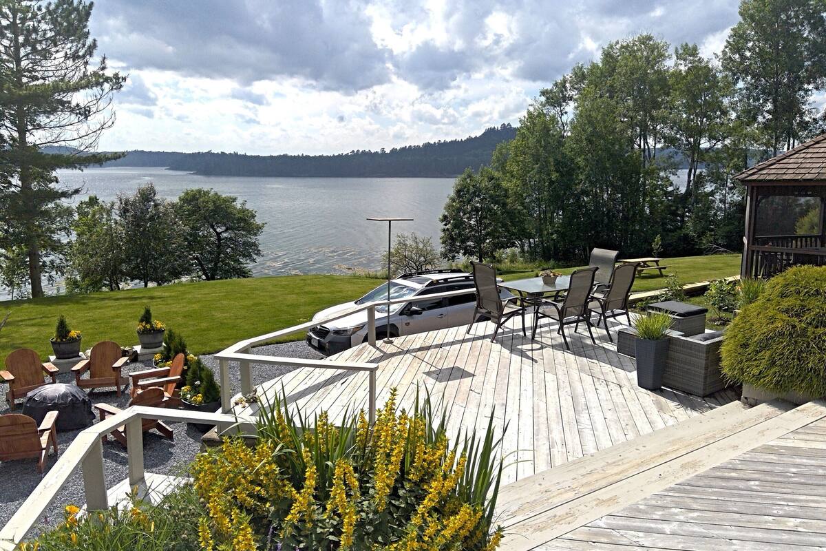 A wooden deck with outdoor seating, overlooking a lake and forested hills.