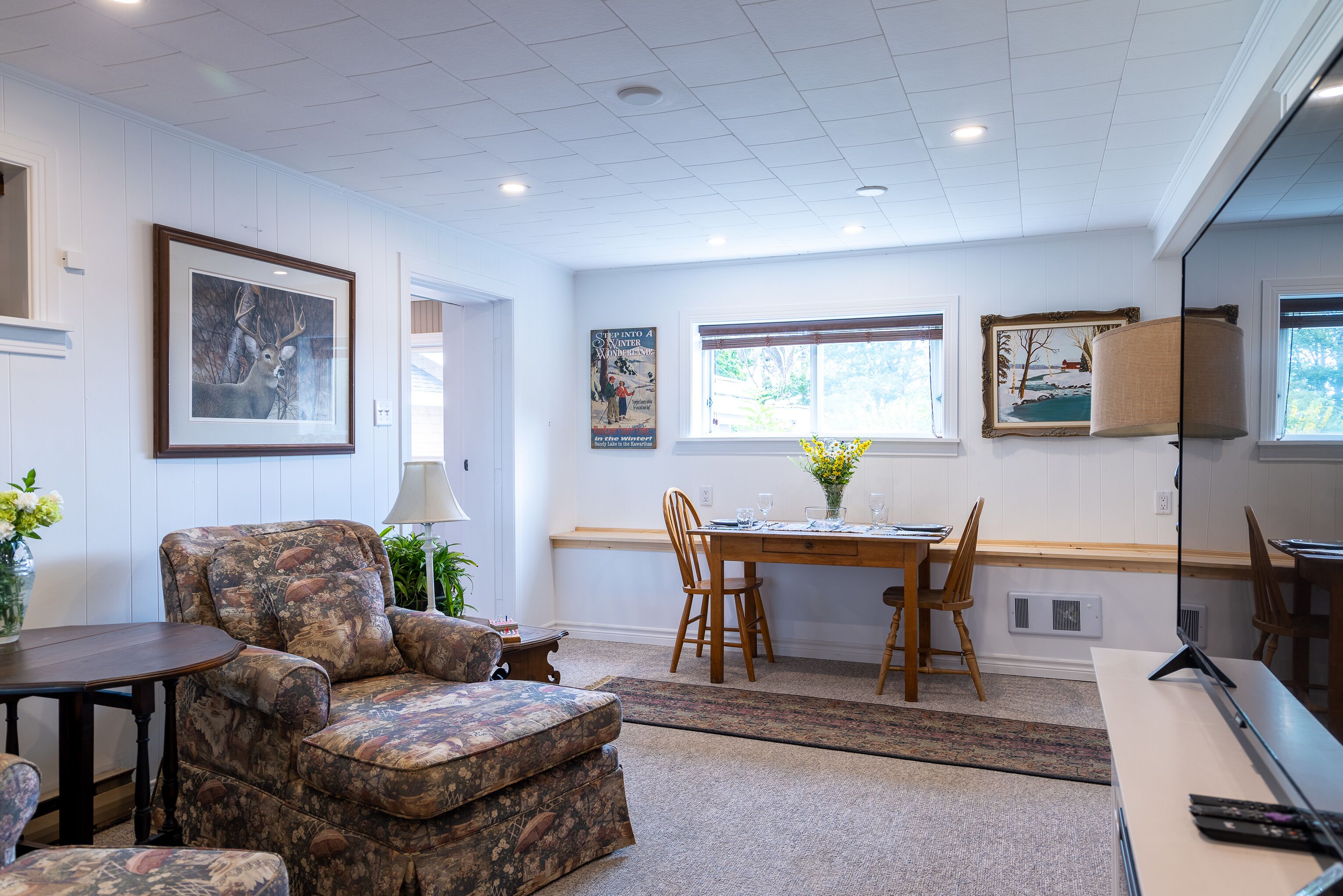 A room with a sofa, a dining table with chairs, a lamp, and framed pictures on the walls.