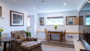 A room with a sofa, a dining table with chairs, a lamp, and framed pictures on the walls.