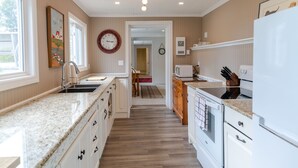 A kitchen with a granite countertop, white cabinets, a wooden floor, and a clock on the wall. - Woodhaven Country Lodge (Oak Bay)