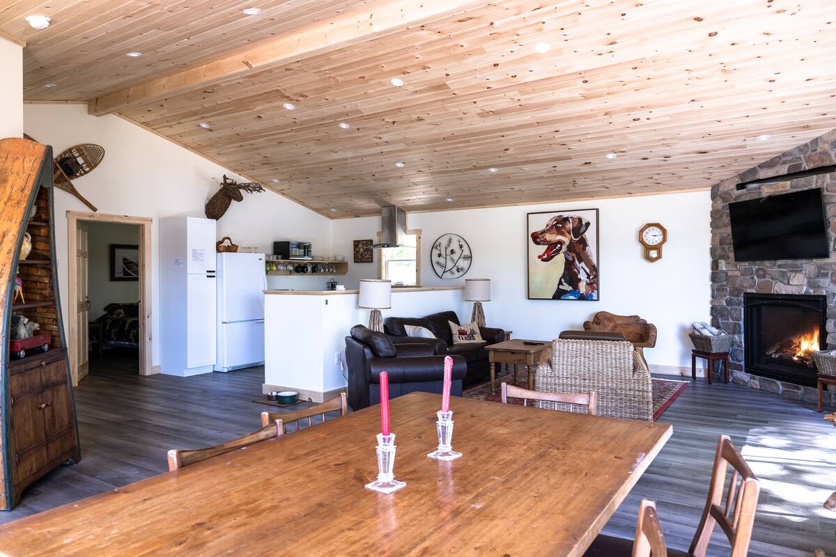 A spacious living area with a wooden ceiling, a stone fireplace, and a dining table with candles.