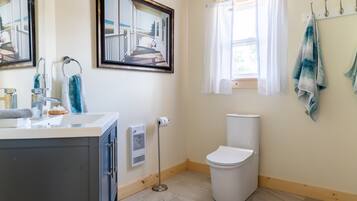 A bathroom with a toilet, sink, and a window with curtains. There are towels hanging on a rack and a mirror on the wall.