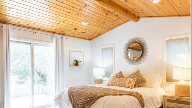 Ein Schlafzimmer mit einem großen Bett, einer Holzbalkendecke, einem runden Spiegel und Blick ins Freie.