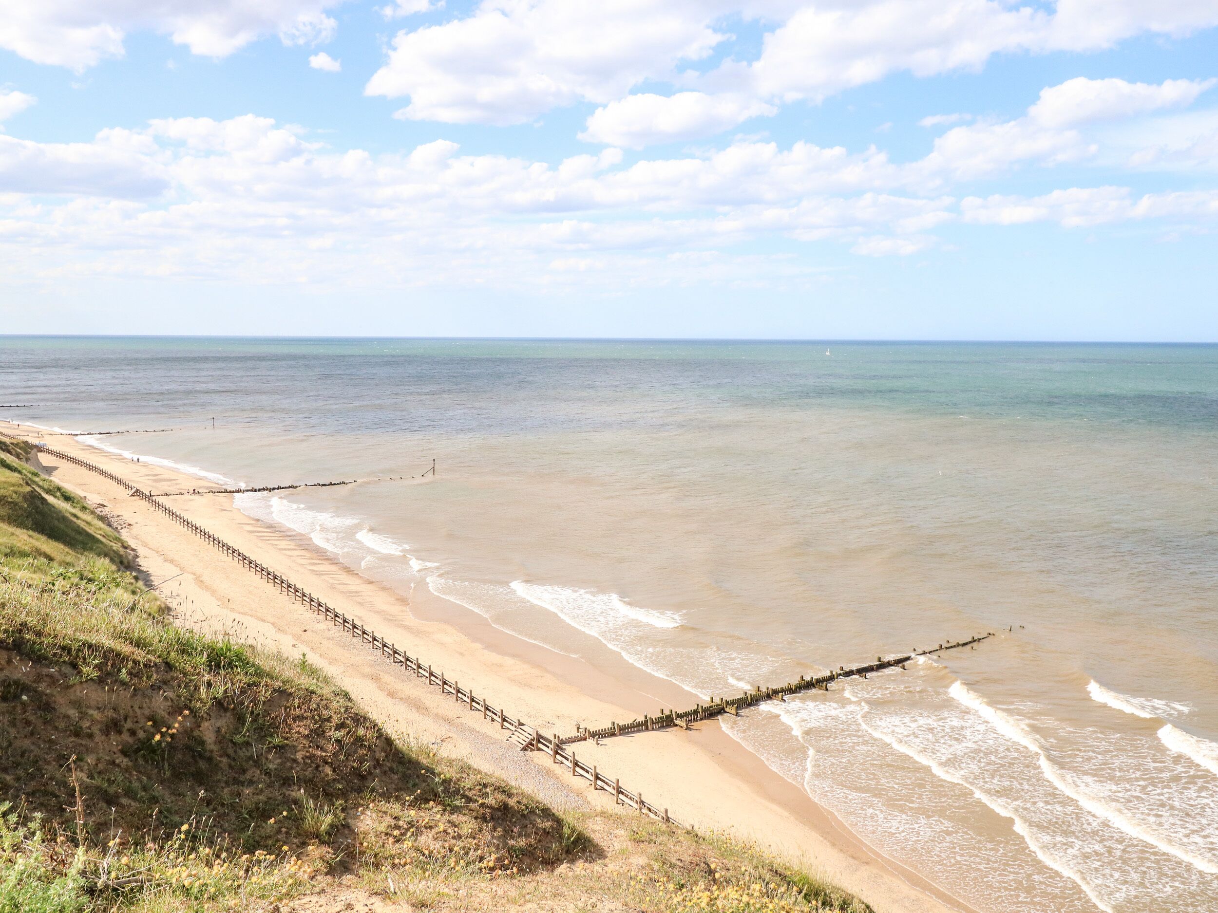 A beach with a wooden walkway along the shore, a clear sky, and calm sea.