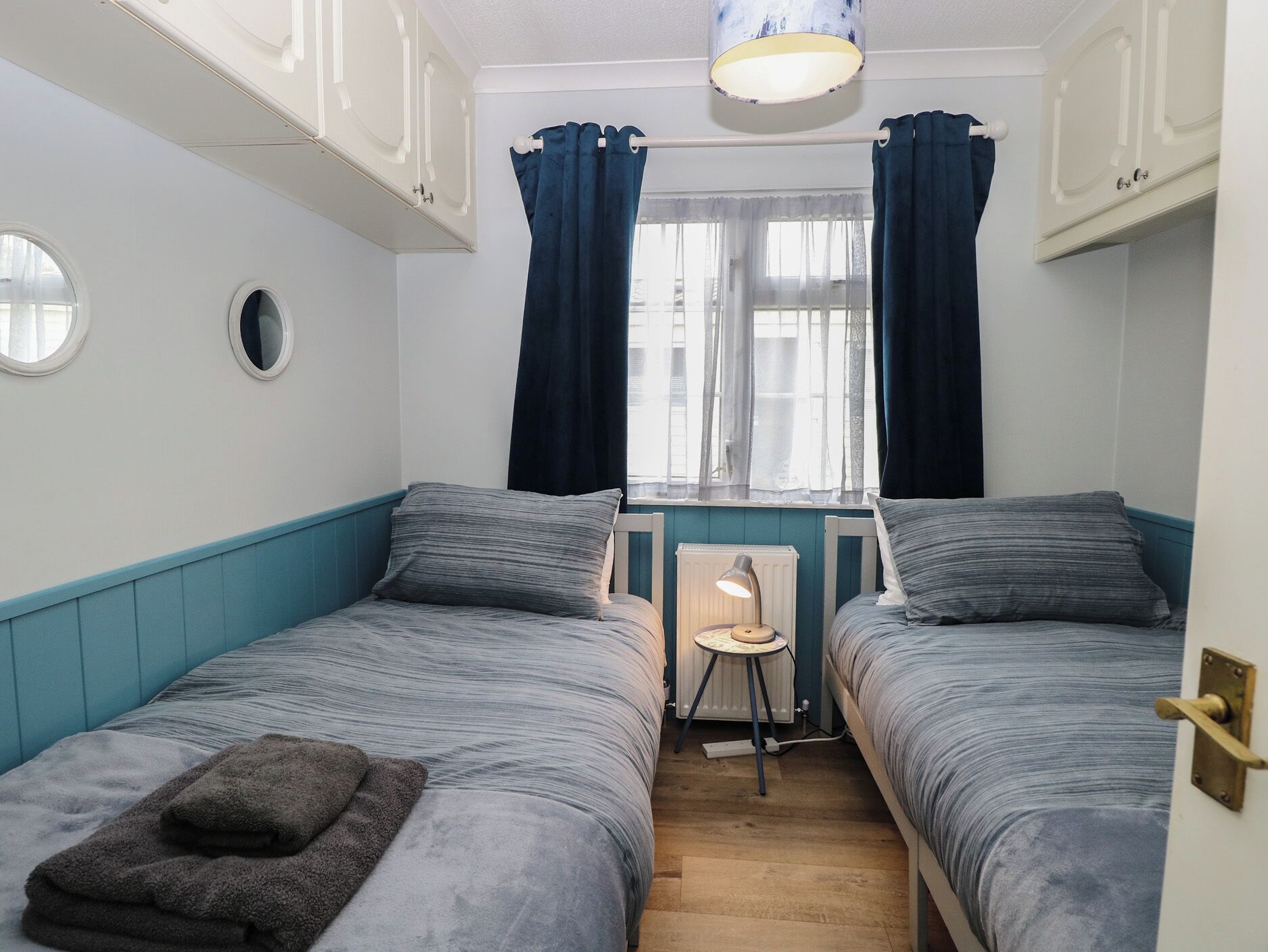 Une chambre avec deux lits, un radiateur, une lampe et une fenêtre avec des rideaux.