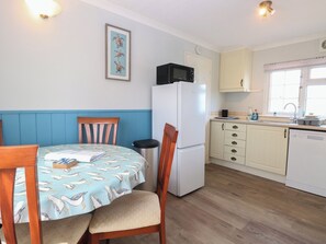 Eine kompakte Küche mit Kühlschrank, Mikrowelle und Spüle. Ein Esstisch mit Stühlen und ein an der Wand hängendes Bild sind ebenfalls vorhanden.
