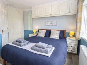 A bedroom with a bed, two bedside tables, a nightstand, a mirror, and a window with curtains.