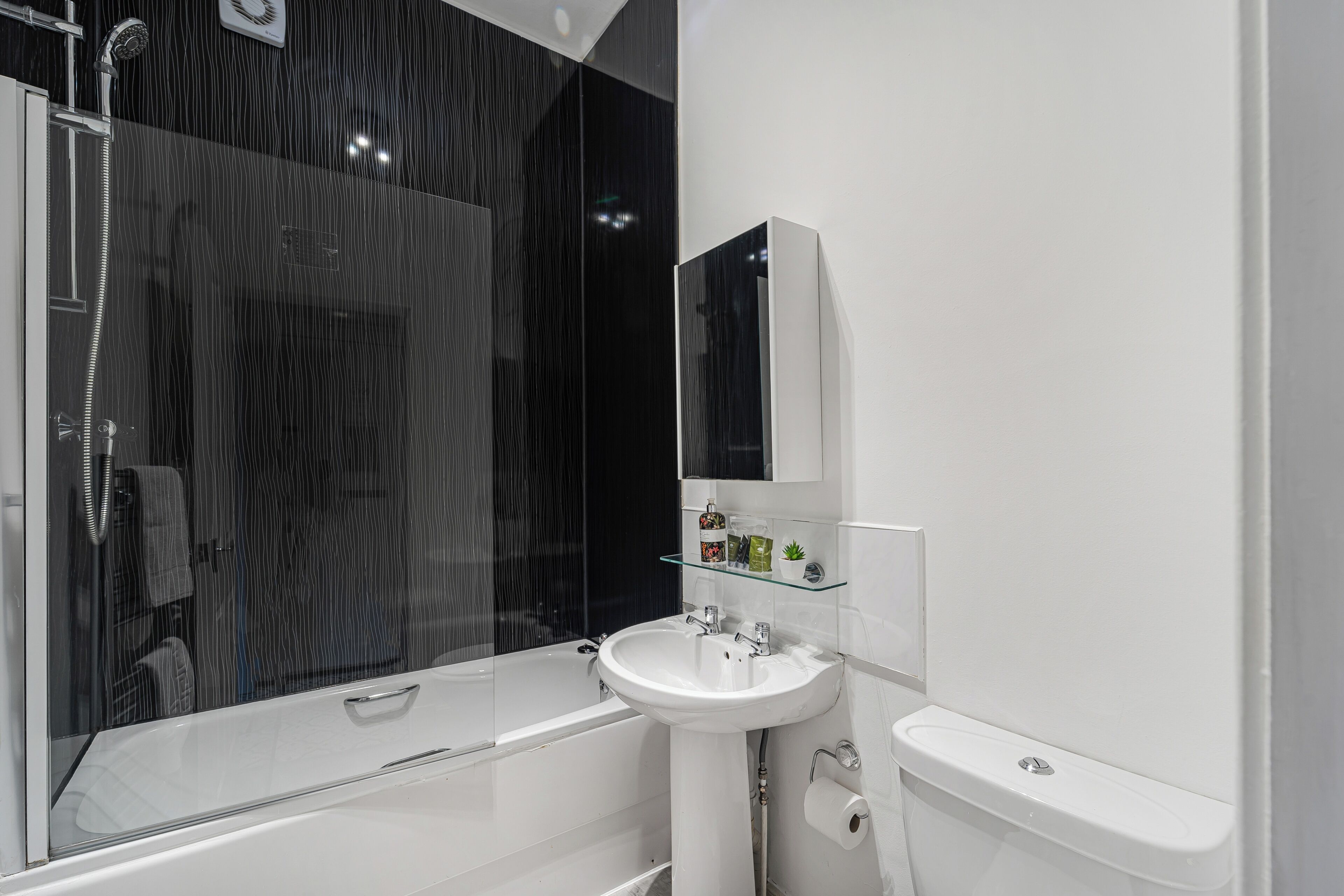 Un baño moderno con ducha envuelta en vidrio, un lavamanos blanco y un inodoro.